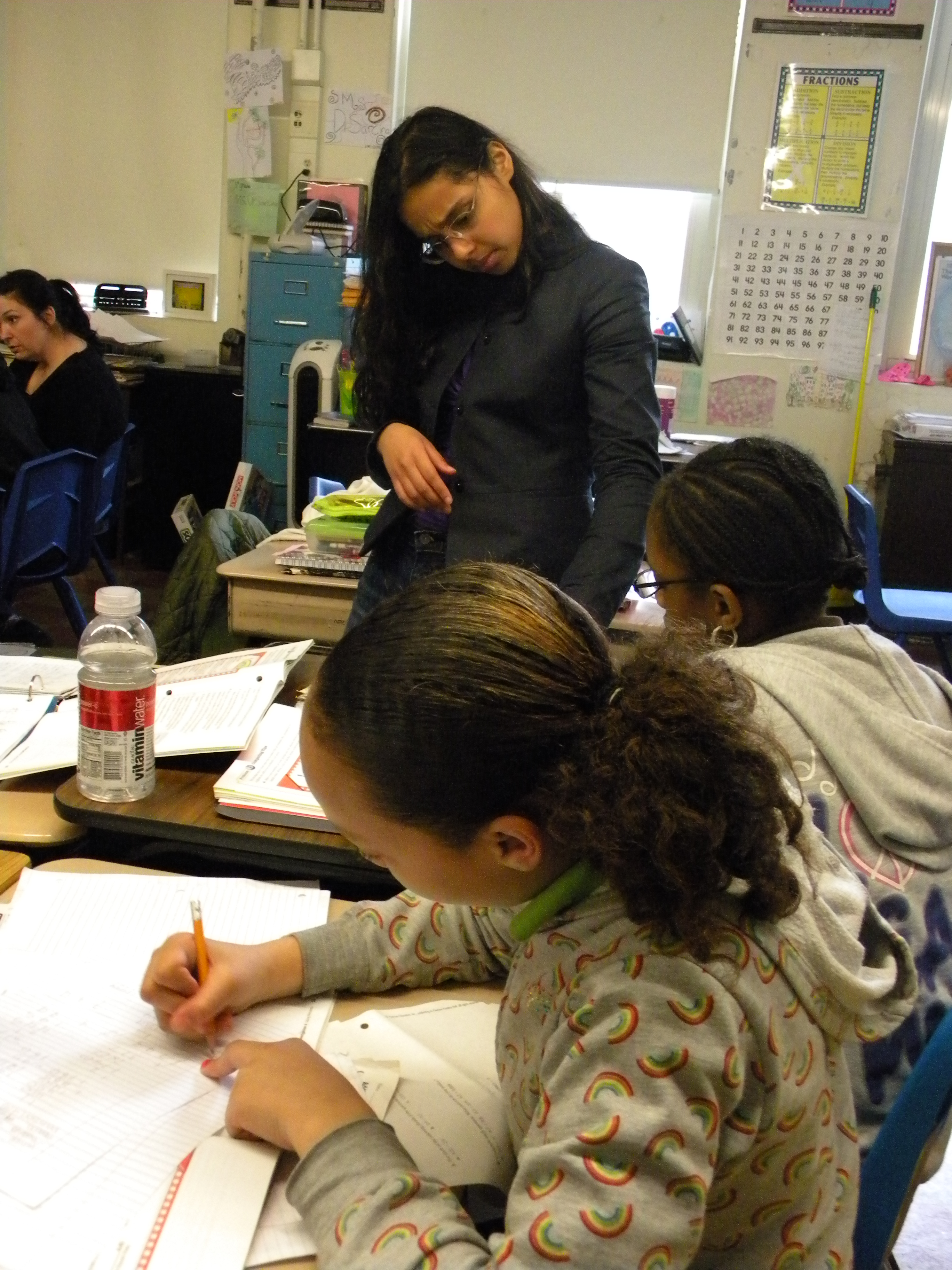 Jolene (foreground) assists a student with a math problem, allowing Ms. DiSarcina (background) to focus her attention on another student. 